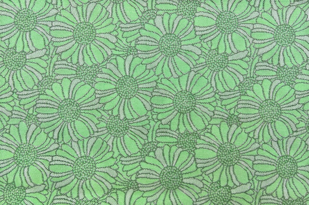 Kissenhülle in grün mit dem floralen „Orakelblume“-Design von Backhausen. Das Muster kombiniert elegante Blumen aneinander- Detailansicht