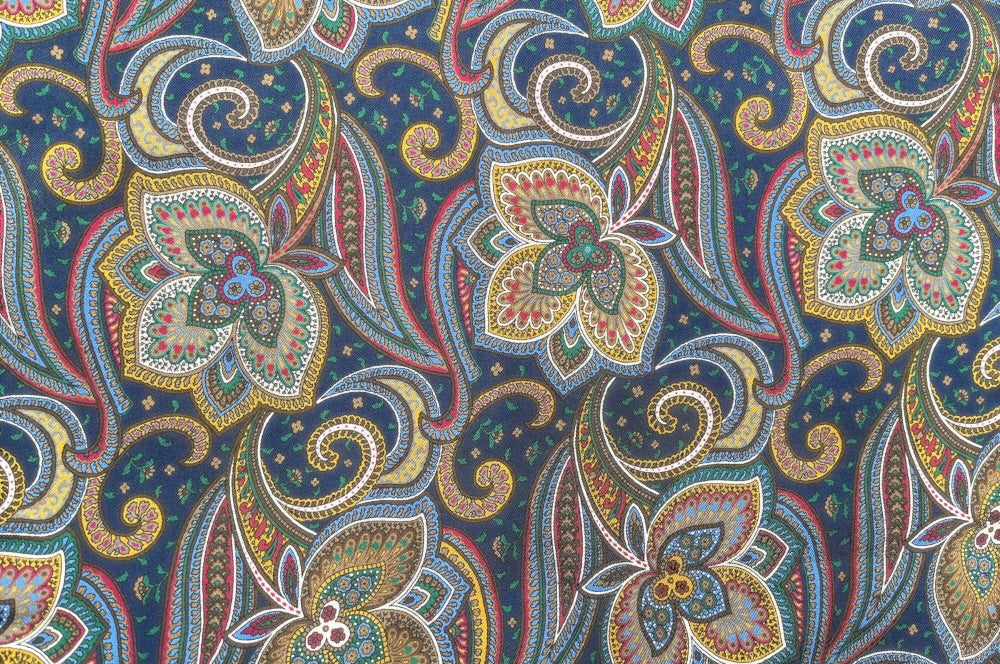 Doppelseitiger Herrenschal mit floralem Seidenmuster in Blau, Rot, Grün und Gelb und einer wärmenden Wollseite in Dunkelblau. detailansicht design