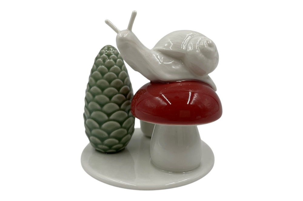 Weißer Herzenhalter mit einer kleinen Schnecke die auf einem roten Pilz sitz, daneben ein grüner ZapfenZapfen, Ansicht von vorne