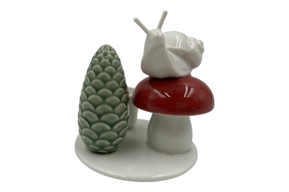Weißer Herzenhalter mit einer kleinen Schnecke die auf einem roten Pilz sitz, daneben ein grüner ZapfenZapfen, Ansicht von vorne