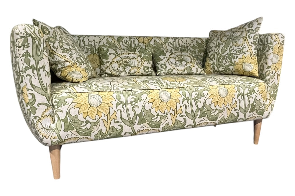 Elegantes Sofa mit geschwungenen Armlehnen und schlanken Holzbeinen. Der Stoffbezug zeigt ein florales Muster mit großen gelben Blumen und grünen Blättern im William-Morris-Stil.